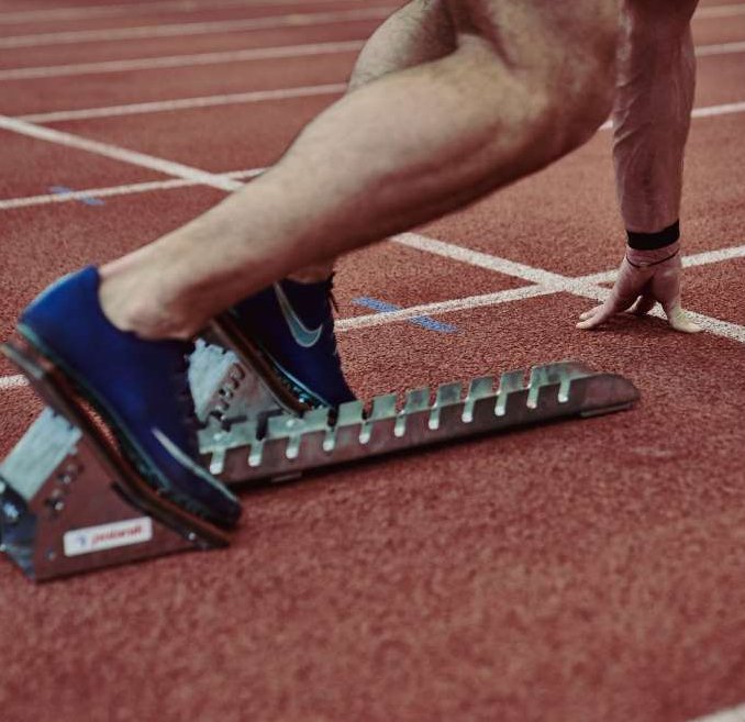 Athlet in Startposition, blaue Laufschuhe im Block, Hand am Boden